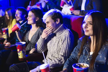 Friends sit and eat popcorn together while watching movies in a movie theater