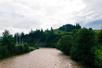 Fototapeta na wymiar Carpathian mountain river in clouny day. Grey and fast water in little stream.Ukrainian village in overcast day. Country side view of cloudy vertex in the middle of summer. Nobody. Season of rain. 