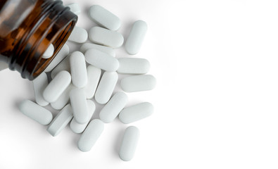 White oval pills near a dark glass bottle isolated on a white background.