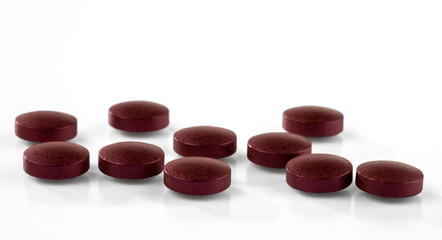 Pills of burgundy color isolated on white background. Selective focus.