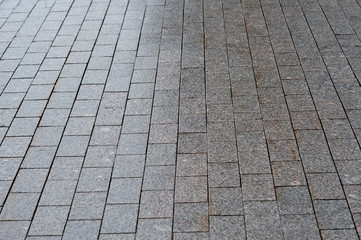 The sidewalk is paved with granite with uneven lighting gradient. Background