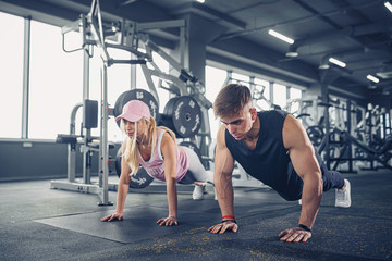 Fototapeta na wymiar Man and woman strengthen hands at fitness training. Fitness young people doing pushups in a gym looking face happy exercise