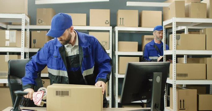 Caucasian postal male worker in uniform packing carton box at delievery department in post office. Postman closing parcel with sticky tape. Mail shipping concept.