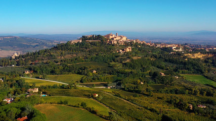 Drone flying over a magnificent authentic Italian cityscape and green meadows. Aerial view of the beautiful medieval old town of Montepulciano with red roofs Tuscany, Italy