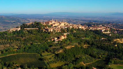 Fototapeta premium Drone flying over a magnificent authentic Italian cityscape and green meadows. Aerial view of the beautiful medieval old town of Montepulciano with red roofs Tuscany, Italy
