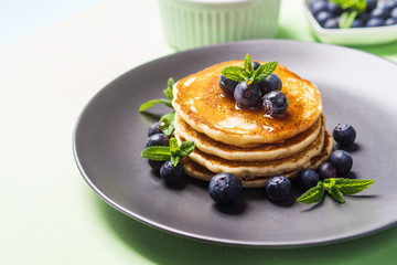 Stack of home made pancakes served with fresh berries and maple syrup on mint green pastel background. Simple and delicious breakfast
