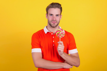 Taste the rainbow. Man candy yellow background. Handsome guy hold candy on stick. Candy shop. Lollipop or sucker. Sugary treat. Candy factory and confectionary