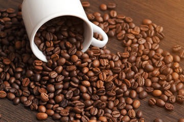 coffee beans are poured from a white Cup on a wooden surface.