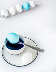Coloring traditional Easter eggs with bright pigment in light-gray crockery on white background....