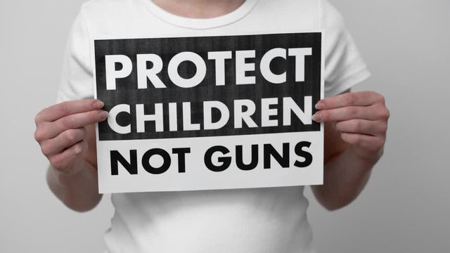 Protect children not guns protest sign in the hands of the young woman in white