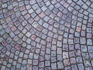 The old stone pavement is lined with the same square blocks in an arc. Cobblestones lie at a certain distance from each other and make up a geometric pattern. Stone background.