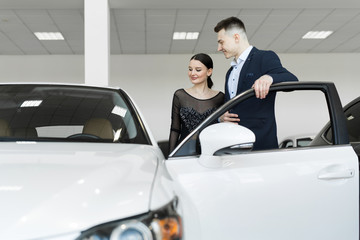 A couple husband and wife choose a car to buy at a car dealership