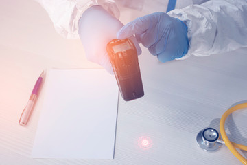 A doctor in a protective biological suit and gloves adjusts the infrared thermometer, top view