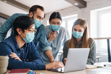 Fototapeta na wymiar Photo of pleased students in medical masks studying with laptop