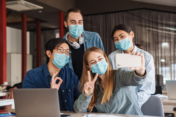 Photo of cheerful students in medical masks taking selfie on cellphone