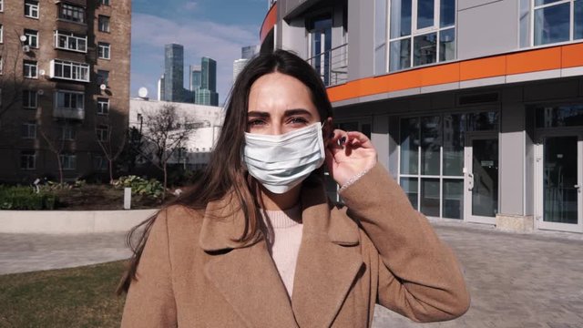 The woman puts on a protective mask and looks at the camera at the city. The concept of health and safety, N1H1 coronavirus, viral protection