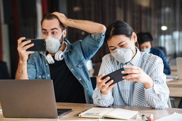 Photo of students in medical masks playing video game on cellphones