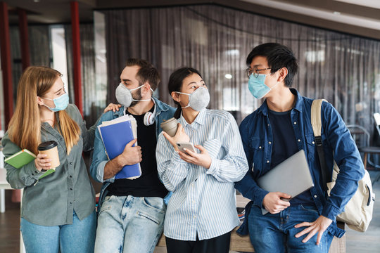 Photo of joyful students in medical masks talking while standing