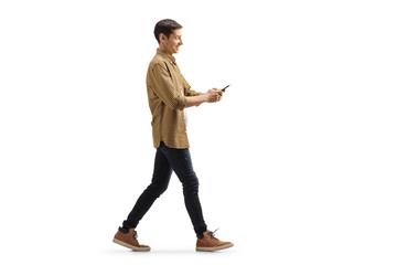 Casual young man in shirt and jeans walking and using a mobile phone