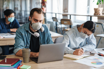 Fototapeta na wymiar Photo of multinational students in medical masks studying with laptop