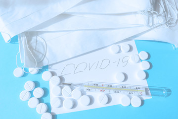 Medical face masks, thermometer and pills on a blue background. The inscription COVID-2019. Concept novel coronavirus.