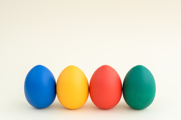 four easter eggs of different colors stay in row in front, white background, copyspace, layout for greeting card, easter holiday concept