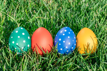 four easter eggs of different colors lay on green spring grass, space for text, celebration of easter holiday, geetings concept