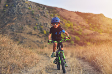 Naklejka premium Happy kid boy of 7 years having fun in autumn park with a bicycle on beautiful fall day. Active child wearing bike helmet