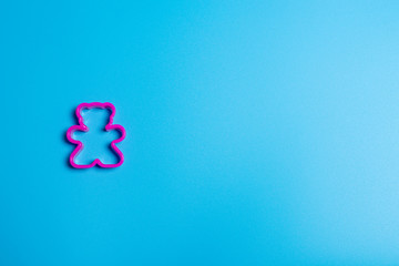 Pink plastic cookie cutter for making cookies in the shape of a teddy bear on a blue background. Culinary concept. Flat lay with copyspace.