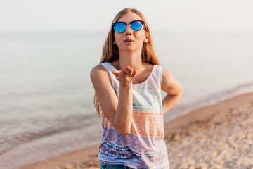 young girl in sunglasses taking a selfie on the beach and sending a kiss