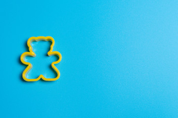 yellow plastic cookie cutter for making cookies in the shape of a teddy bear on a blue background....