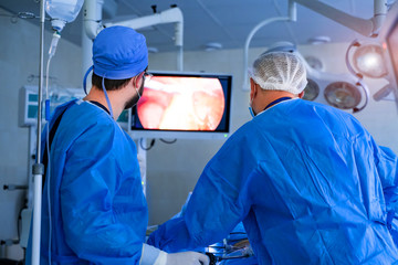 Group of surgeons men working with modern equipment. Back view of team of specialists in special...