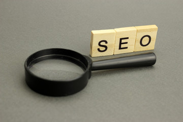 SEO lettering in wooden letters and a magnifying glass on a grey background