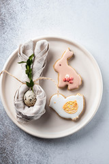 Table setting for the holiday of Easter. The photo shows white dishes, serving mat, Easter egg in a napkin. Napkin draped under rabbit ears.