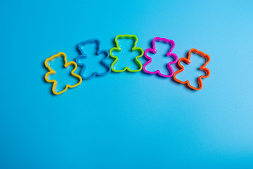 Five multi-colored plastic cookie cutter for making cookies in the shape of a teddy bear on a blue...