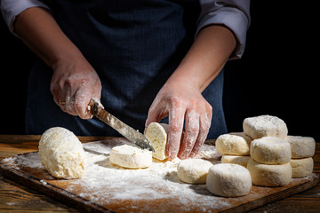 Female hands knead the dough on a wooden antique table on a dark background, close-up, shallow depth of field, beautiful directional lighting. Concept of home baking and comfort.
