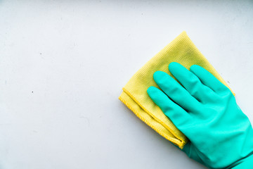 hand in rubber glove wipes dust with a rag from a white window sill or table