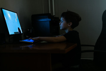 child boy plays computer games in a dark room