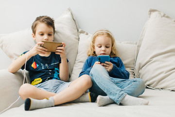 2 children a boy and a girl sit on gadgets and play phones in the afternoon