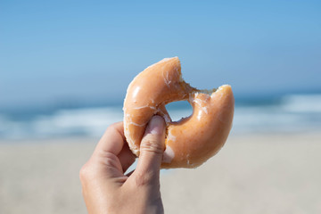 Hand holding bite Donut on beach background.