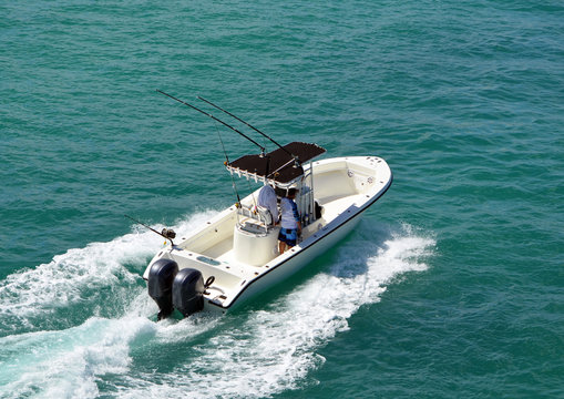 Angled overhead view of an open sport fishing boat with a black canvas canopied center console powered by two outboard meninges.