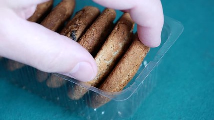 Oatmeal cookies lie in transparent open plastic tray. Male hand takes sweet ruddy cookies. Concept of overeating and abuse of carbohydrate-rich foods. Glycemic foods that increase blood insulin levels