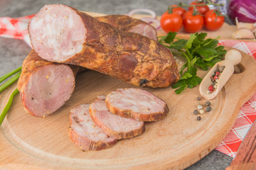 Sausage with minced meat, cut into small pieces on a wooden board with spices and herbs. Close-up
