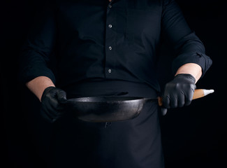 male cook in black uniform and latex gloves holds an empty round vintage black cast iron pan