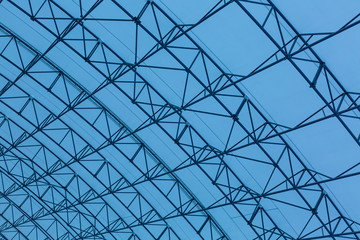 Glass roof in the form of triangles on the background of the blue sky. The roof of an office building, a shopping center. Reflection of the sky.