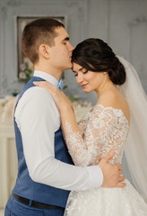 Happy groom kisses the bride hugging her waist in a vintage interior. Beautiful elegant couple of newlyweds in love. Wedding concept. Happy newlywed couple.