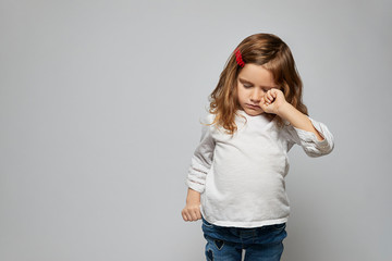A young girl rubs her eye with a knuckle