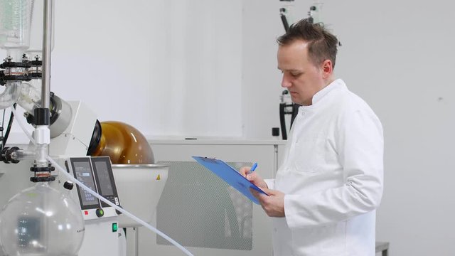 Chemist inspecting rotavapor machine in laboratory and writing down results.