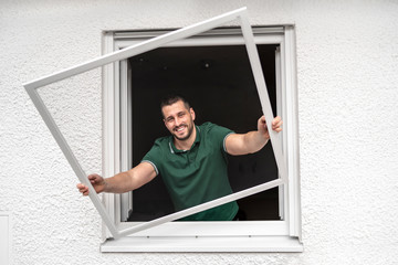 freundlicher Handwerker montiert Insektenschutzgitter bei einem Kunden zu Hause