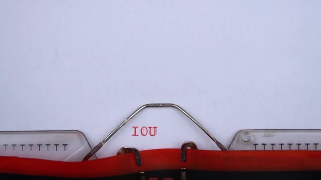 IOU - abbreviation printed on an old typewriter in red letters, close up. I owe you, vintage inscription